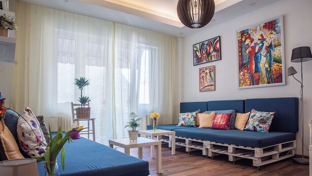 Uma sala de estar acolhedora com um sofá azul, mesa de centro de madeira e uma pequena mesa com um vaso de flores.
