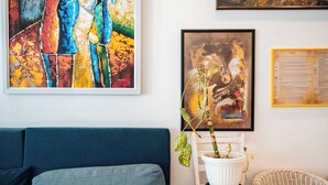 Um quarto com um sofá azul, uma mesinha de cabeceira branca com uma planta em vaso, e duas obras de arte emolduradas na parede.