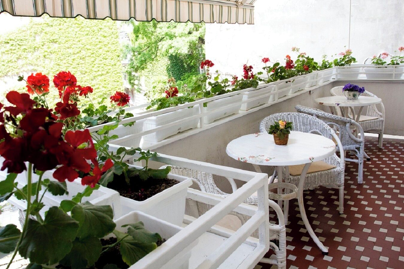 Un patio couvert aménagé avec des meubles en osier blanc et des plantes en pot.
