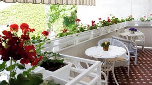 Uma área de varanda coberta com móveis de vime branco e plantas em vasos.