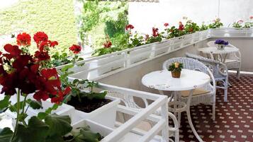 Un patio couvert aménagé avec des meubles en osier blanc et des plantes en pot.