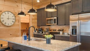 A modern kitchen with granite countertops, stainless steel appliances, and wooden cabinetry. - NEW! Indoor Pool Retreat - Sugar Maple Splash w/ Hot Tub (Sevierville)
