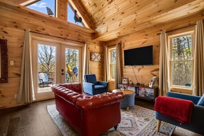 L’intérieur d’un chalet en bois, avec un canapé en cuir rouge, un fauteuil bleu et un téléviseur à écran plat.