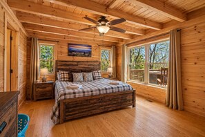 Camera da letto in una baita di legno con un letto, una ventola a soffitto e ampie finestre.