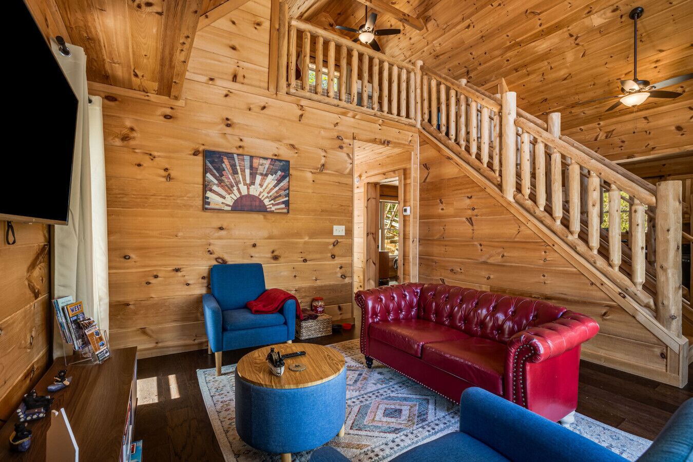 A wooden interior with a staircase, a blue armchair, a red leather sofa, and a round wooden coffee table.