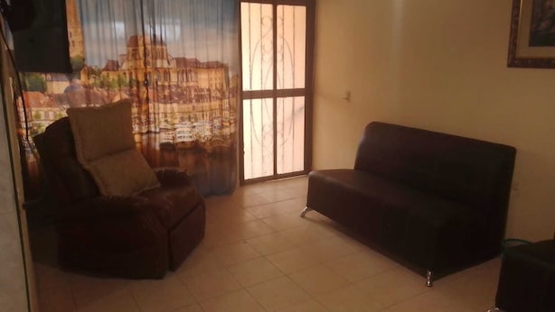 A living room with a sofa, a chair, and a large window with a view of buildings. - Alojamiento Olsi (Torreón)