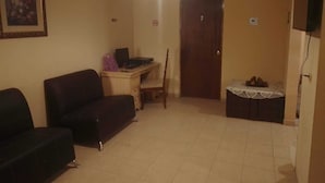 A living room with a sofa, a desk with a computer, a door, and a small table with fruits. - Alojamiento Olsi (Torreón)