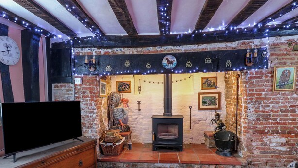 A cozy living room with exposed brick walls, a traditional fireplace, and a large flat-screen TV. - Driftway Stables Retreat (Diss)