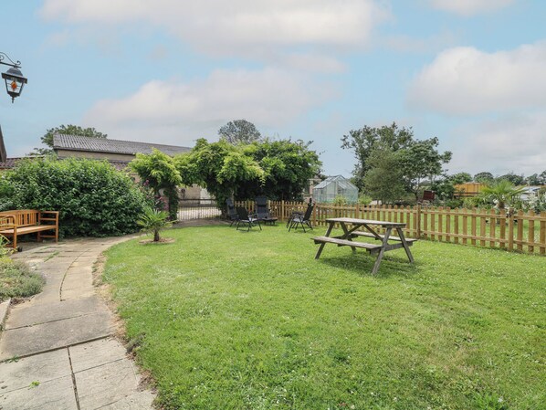 A backyard with a wooden bench, a picnic table, and a garden area with a hedge and a small tree.