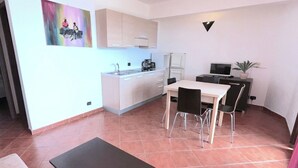 A compact living space with a kitchenette, a dining area with chairs, a small table, and a painting on the wall.