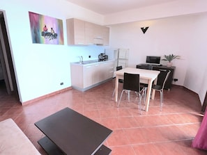 Un espacio habitable compacto con kitchenette, una zona de comedor con sillas, una mesa pequeña y un cuadro en la pared.