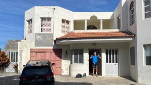A two-story building with a car parked in front, a person standing at the entrance, and a sign with 'APC' on the side.
