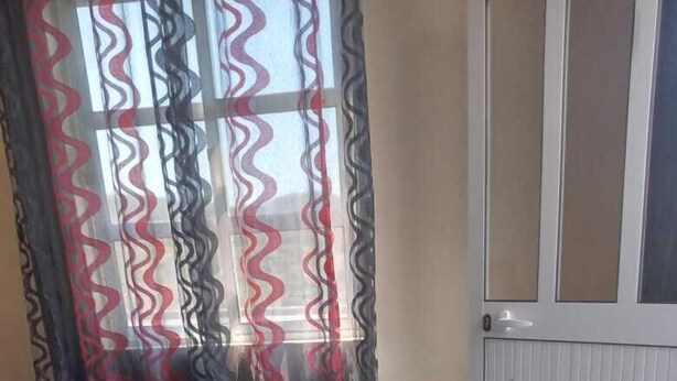 A room with a bed, a window with patterned curtains, and a door.
