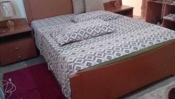 Un dormitorio con una cama de madera, dos mesitas de noche, un velador, una alfombra roja y un cuadro enmarcado en la pared.