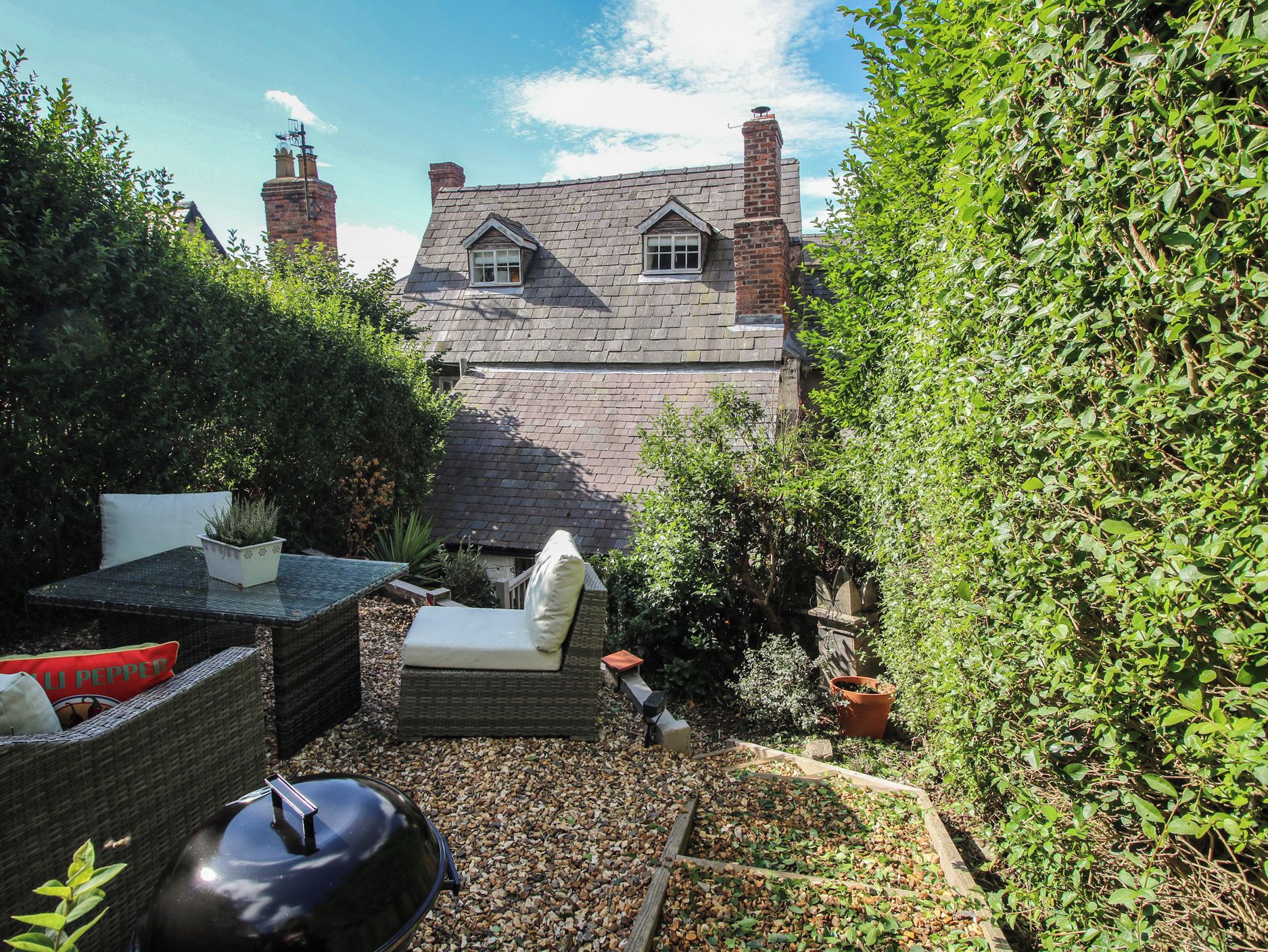 A garden with a stone house, outdoor furniture, and a variety of plants.