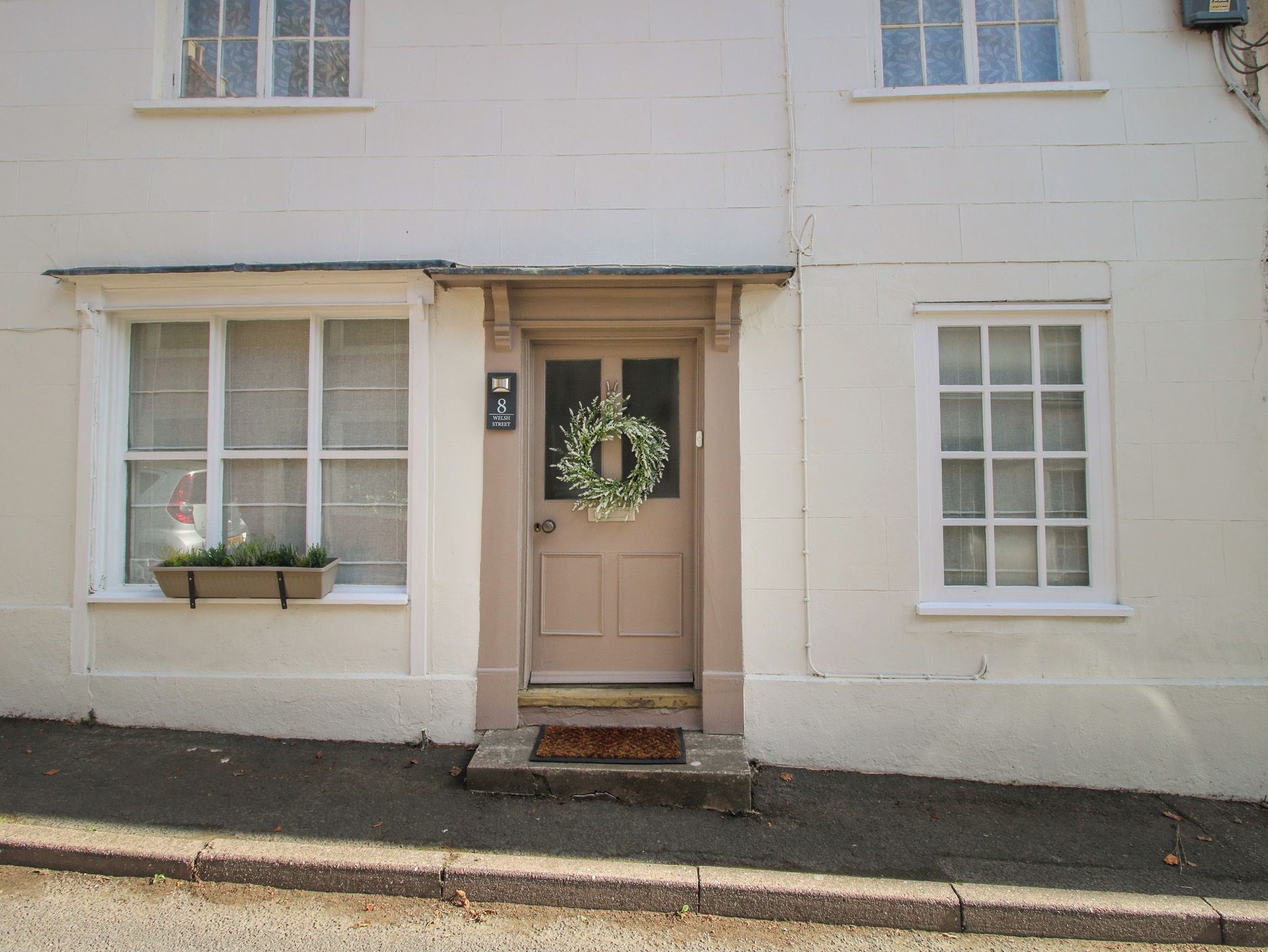 A building with a beige door, a wreath, and a window with a planter.
