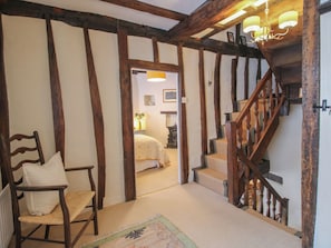 A traditional room with exposed wooden beams, a wooden chair, a bed, and a staircase with a wooden railing. - 8 Welsh Street (Bishops Castle)