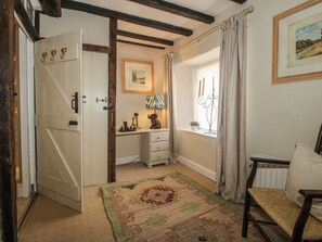 A room with a wooden door, a desk with a lamp, a chair, a window with curtains, and a framed picture on the wall. - 8 Welsh Street (Bishops Castle)