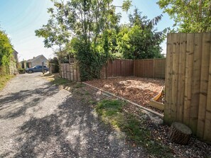 A gravel driveway leading to a wooden fence, a car parked on the street, and a house in the background. - 8 Welsh Street (Bishops Castle)