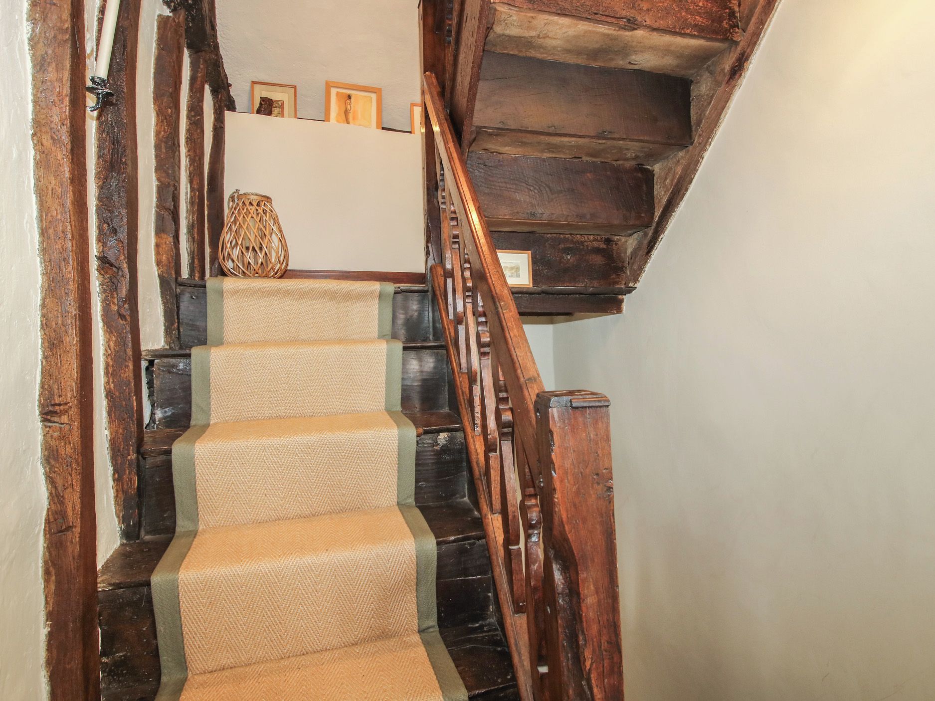 Un escalier en bois, avec une moquette tissée et un panier en osier posé sur la plateforme.