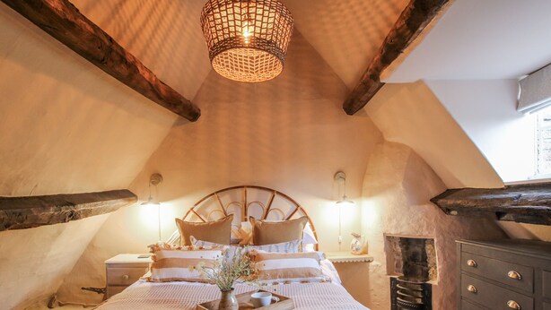Ein gemütliches, rustikales Schlafzimmer mit einer gewölbten Decke, einem hölzernen Bettgestell, einem Nachttisch mit Lampe und einer Kommode.