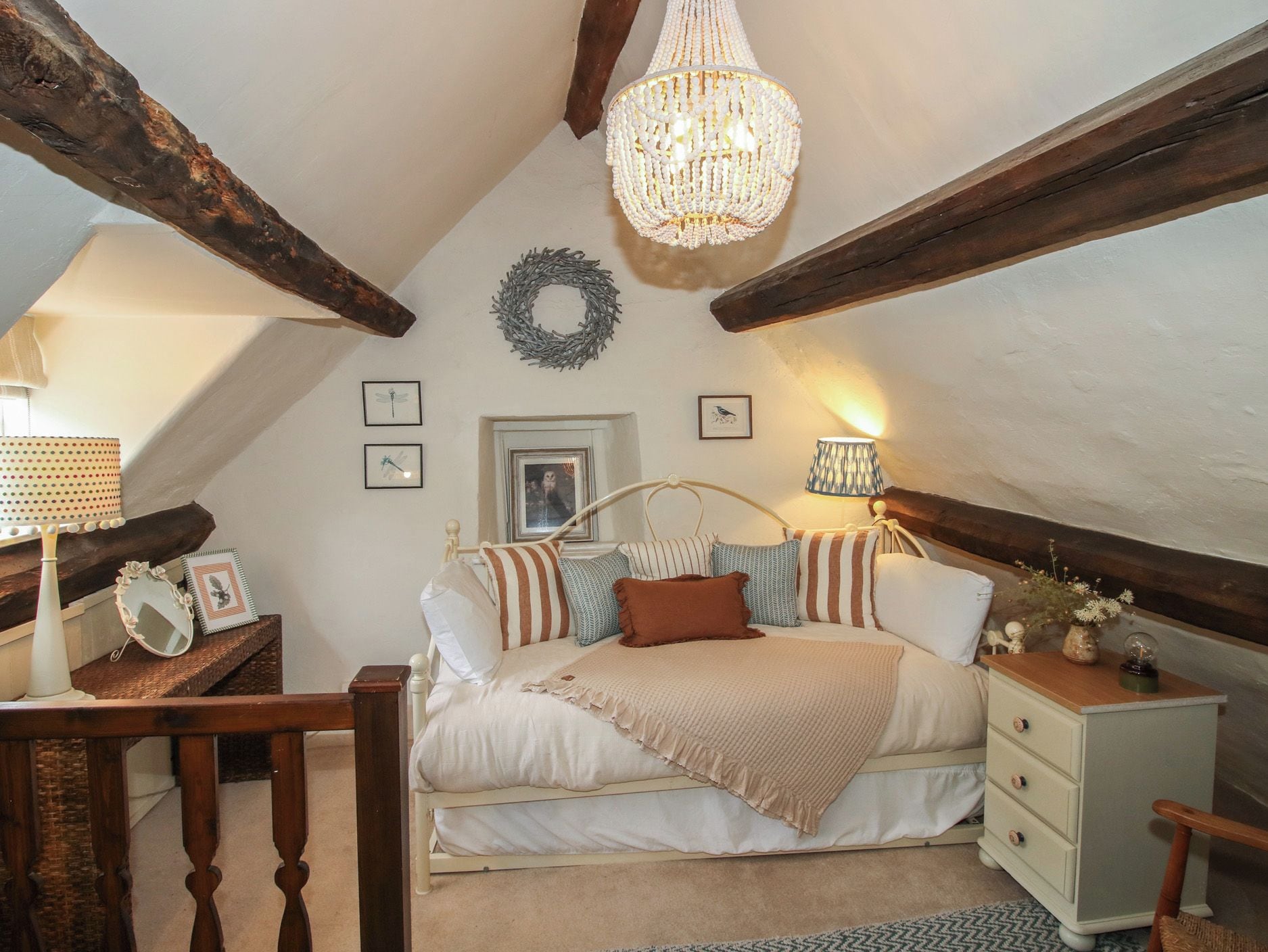 A cozy bedroom with a sloped ceiling, a chandelier, a bed with striped pillows, a nightstand, and a dresser.