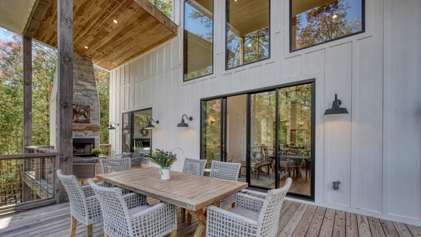 Une terrasse en bois avec une table et des chaises, une cheminée en pierre et de grandes fenêtres.