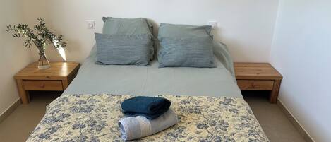 A bed with a floral quilt, two pillows, a vase with a plant, and two wooden nightstands.