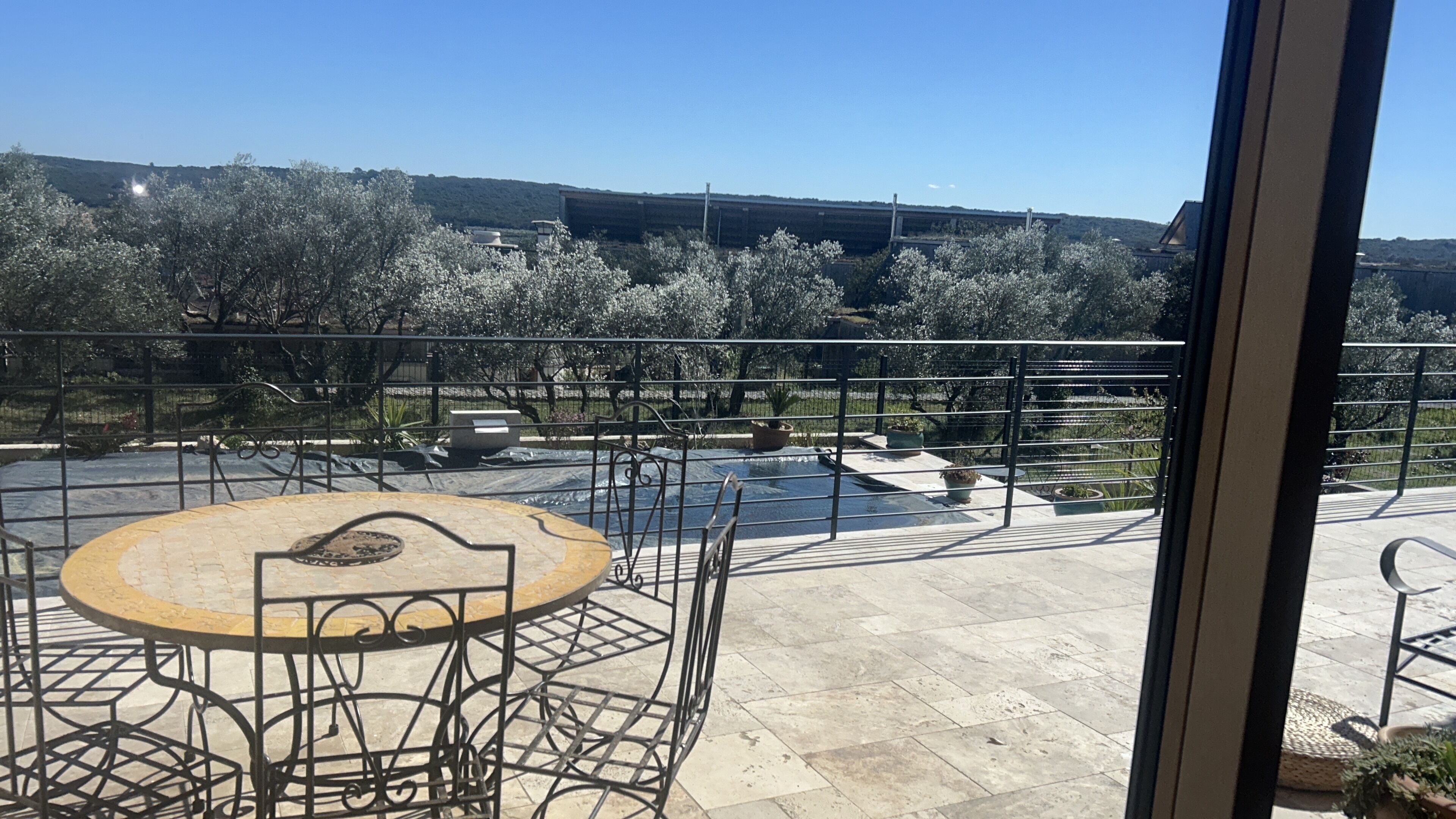 Eine Terrasse mit einem runden Tisch und Stühlen, einem kleinen Brunnen und Blick auf Bäume und Hügel.