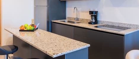 Una cocina compacta con encimera de granito, microondas integrado, cafetera y refrigerador.