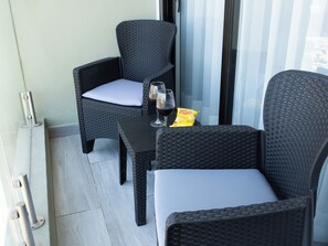 Ein Balkon mit zwei Korbstühlen, einem kleinen Tisch, zwei Weingläsern und einer Snacksnackpackung.