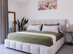Ein modernes Schlafzimmer mit einem großen Bett, einem Kopfteil, einem Nachttisch, einer Lampe und einer Topfpflanze.
