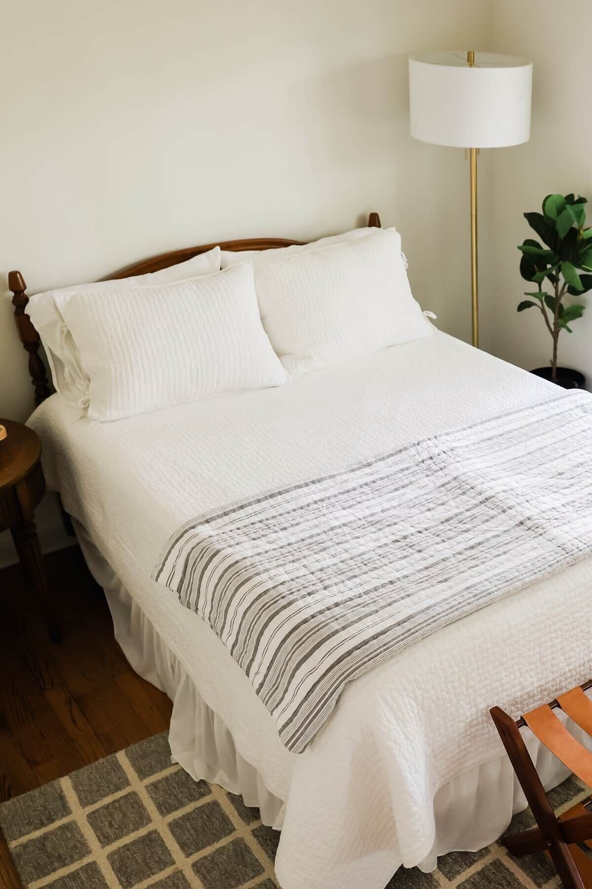 Un letto ben rifatto con un piumone bianco, una coperta a righe e una testiera in legno.