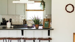 A modern kitchen with white cabinets, a black countertop, and a hanging plant. There are three stools and a wooden chair. - Walton House (College Station)