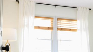 A bedroom with a bed, a bedside lamp, and a window with curtains. - Walton House (College Station)