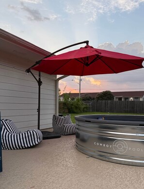 A backyard with a hot tub, striped bean bag chairs, and a red umbrella. - Walton House (College Station)