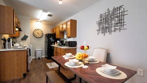 A modern kitchen with wooden cabinets, a dining table set with white plates and bowls, and a fruit bowl on the table.