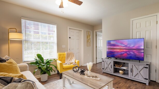 A living room with a sofa, yellow armchair, TV, and a ceiling fan.