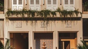 A two-story building with a tiled entrance, a central fountain, and potted plants.