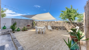 Eine Terrasse mit Tisch und Stühlen, einem Sonnensegel und Kübelpflanzen.