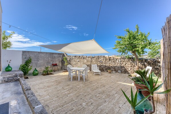 Une terrasse avec une table et des chaises, un auvent et des plantes en pot.