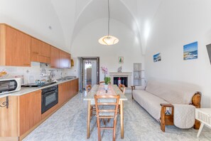 A modern kitchen with wooden cabinets, a dining table, and chairs. There is a sofa and a fireplace in the living area. - Da Lu Pira – Cozy Apartment in the Heart of Salento (castrignano del capo)