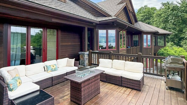 Eine Holzterrasse mit Gartenmöbeln, einem Kamin aus Stein und Blick auf einen See.