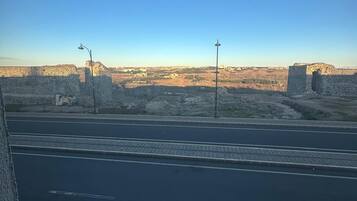 Et gadesyn med en hvid bil parkeret til siden, en klar blå himmel og et fjerntliggende vue af en stor, historisk murstensmur.