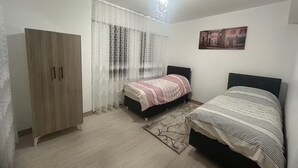 Ein Schlafzimmer mit zwei Betten, einem Kleiderschrank, einer Chandelüster und einem Fenster mit durchsichtigen Vorhängen.