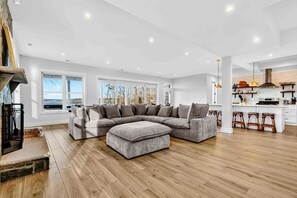 A modern living room with a sectional sofa, wooden flooring, and a kitchen area with bar stools. - Lakefront Lake Anna, Hot Tub, Boat Dock (Mineral)