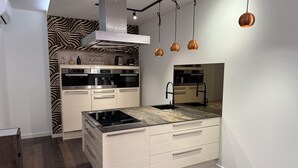 Et moderne køkken med en central ø, indbyggede apparater og hængende lamper.