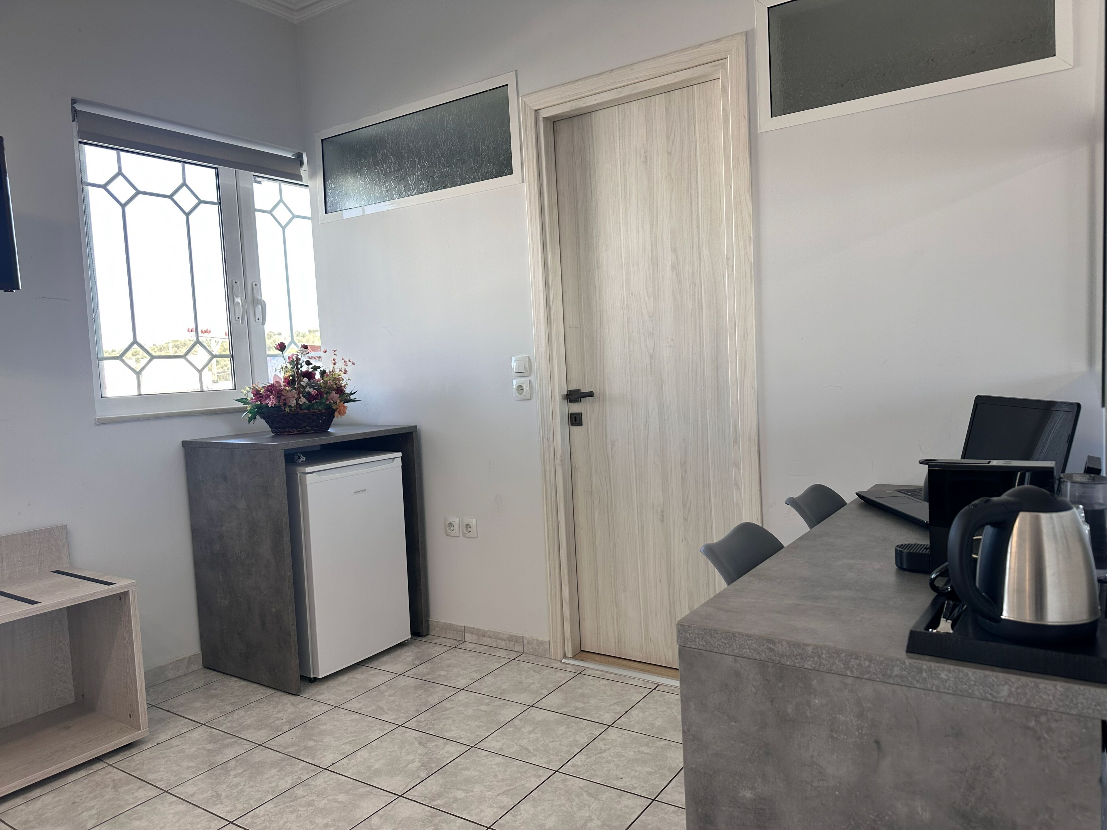 A compact kitchen with a refrigerator, a sink, a countertop, a window with a decorative grille, and a door.