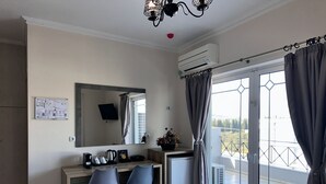 A hotel room with a desk, two chairs, a mirror, a small refrigerator, a coffee maker, a plant, and a balcony with a view. - Airport Suites Michelle (Spata-Artemida)
