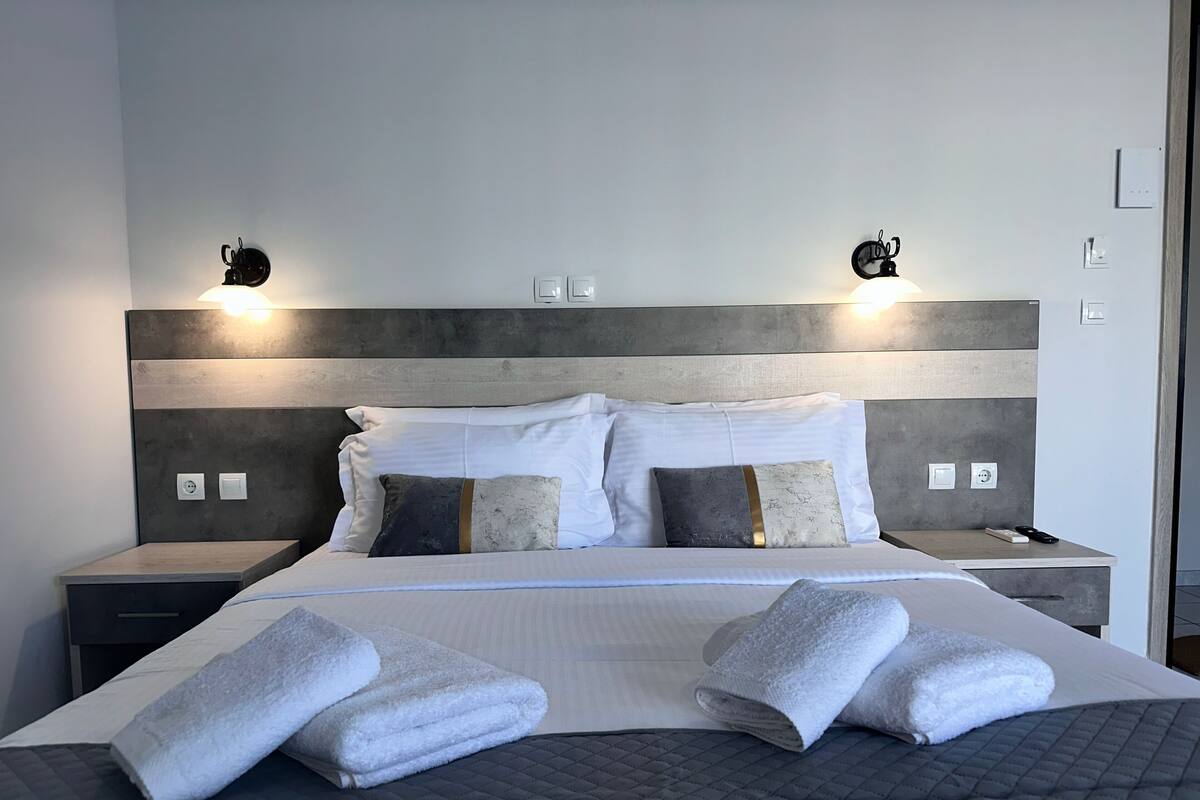 Ein ordentlich bezogenes Bett mit zwei Kissen, ein Nachttisch mit Fernbedienung und zwei Wandleuchten.